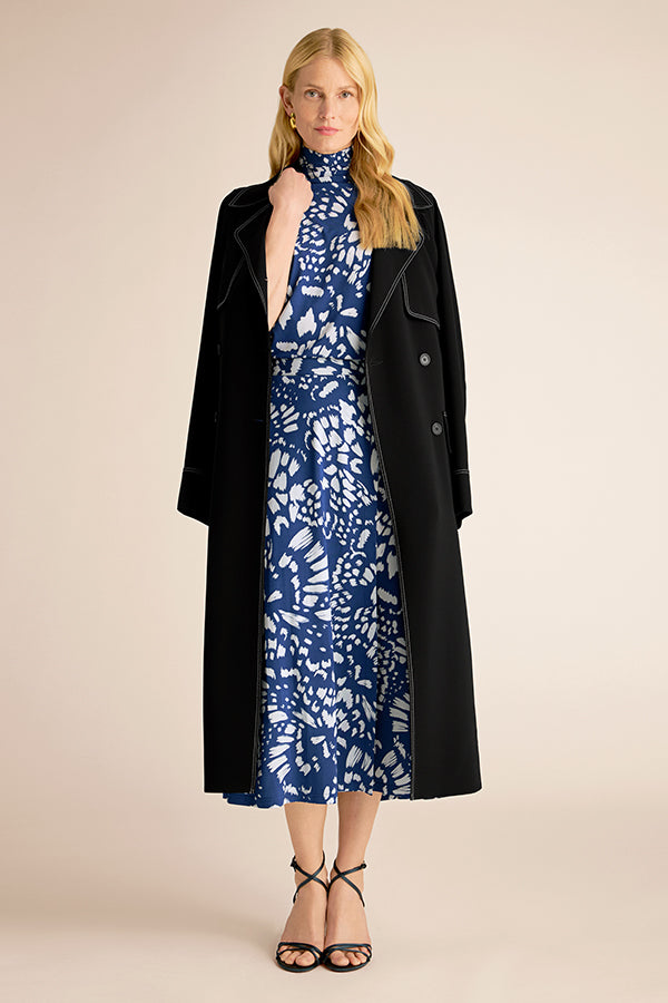 Woman wearing a blue floral dress with a black coat on a beige background | Exclude
