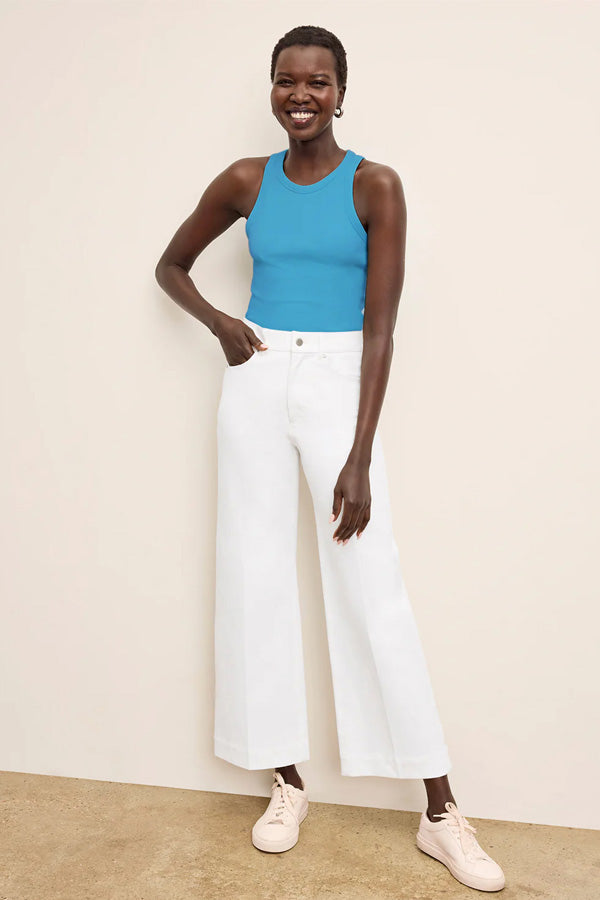 Woman wearing a blue tank top and white pants against a beige background | Exclude | Grid