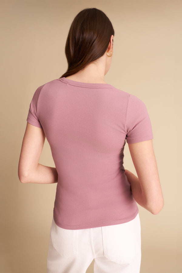 Woman wearing a mauve t-shirt and white pants against a beige background | Exclude