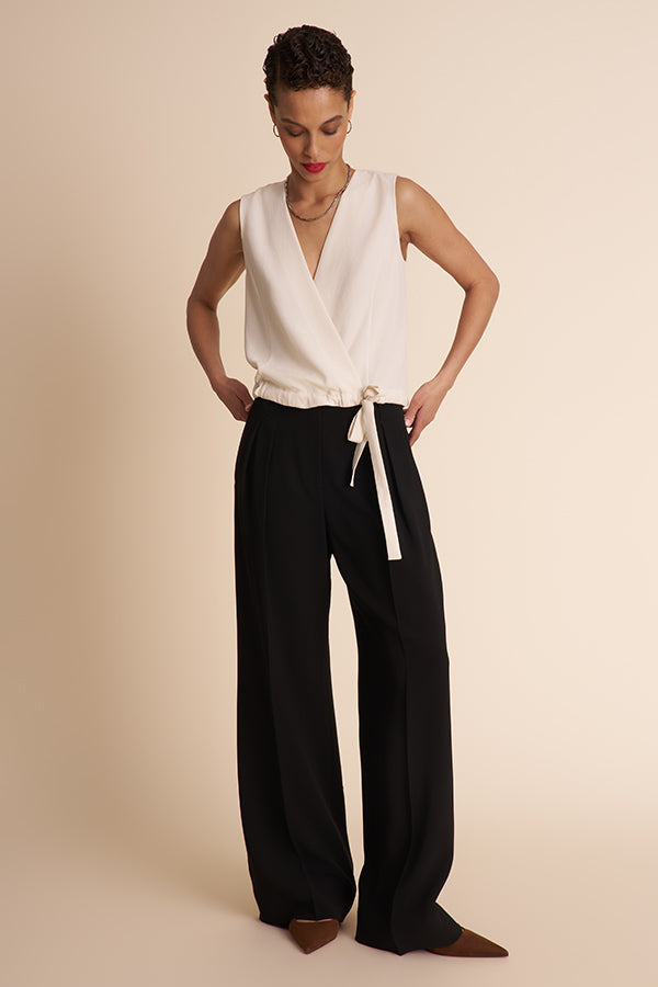 Woman wearing a white sleeveless top and black wide-leg pants on a beige background | Exclude | Grid Hover