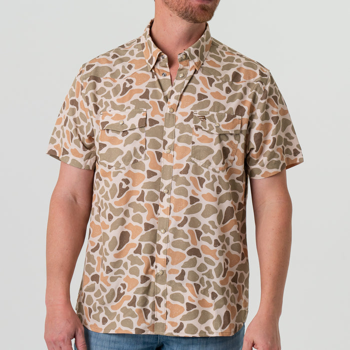 Person wearing a short-sleeve shirt with a camouflage pattern on a plain background