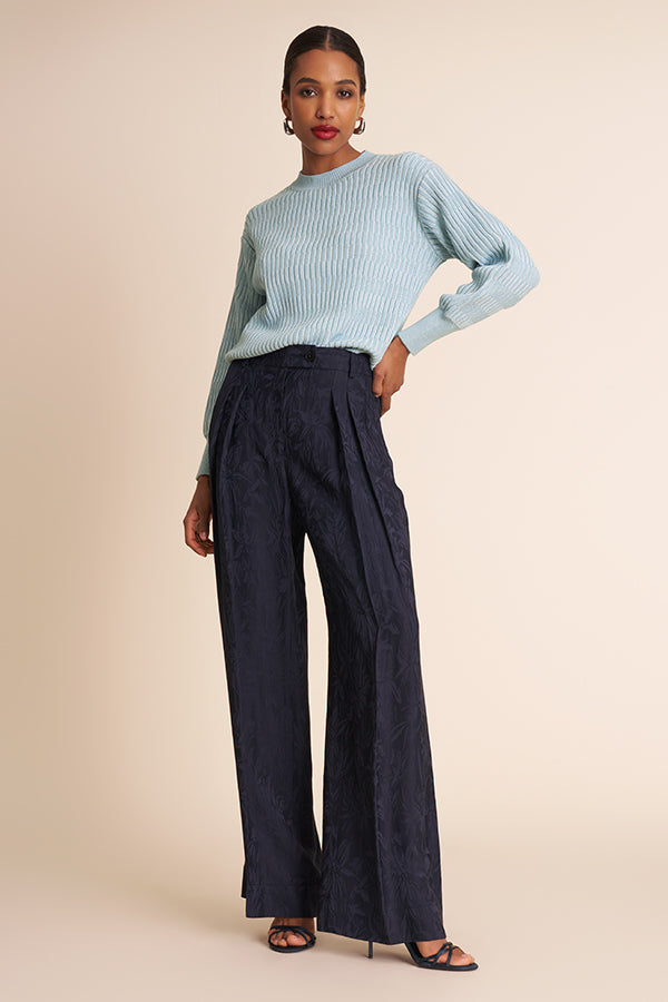 Woman wearing a light blue sweater and dark blue wide-leg pants on a beige background | Exclude