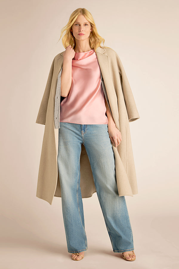 Woman wearing a beige coat, pink top, and blue jeans on a beige background | Exclude
