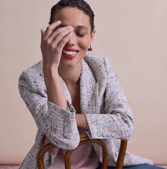 Woman sitting on a chair with one hand covering her face against a beige background