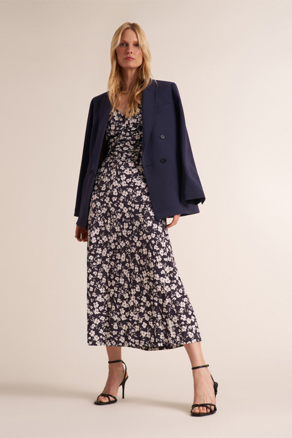 Woman wearing a navy and white floral dress with a navy blazer draped over her shoulders | Exclude