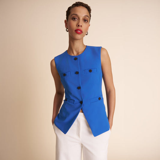 Woman wearing a blue vest with black buttons on a beige background | Lead