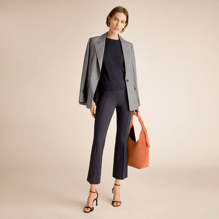 Woman in gray blazer and black pants holding an orange bag on a beige background