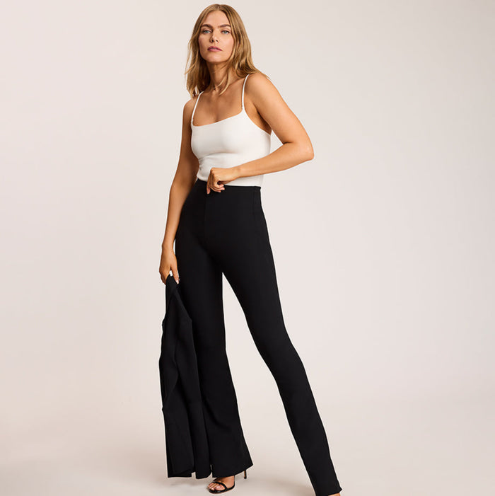 Woman wearing a white bodysuit and black high-waisted pants on a plain background | Exclude