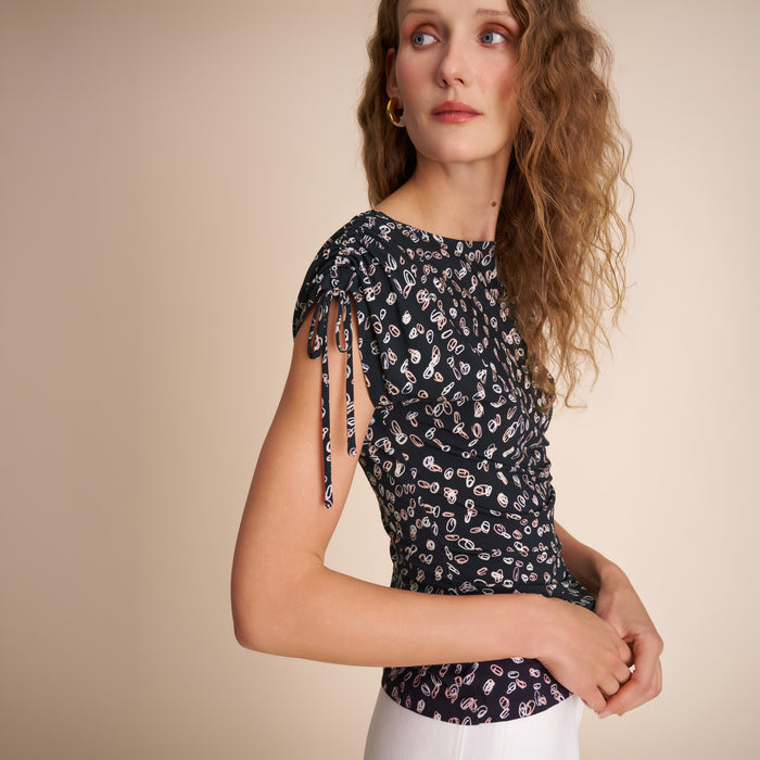 Woman wearing a black floral top with tied sleeves against a beige background | Lead