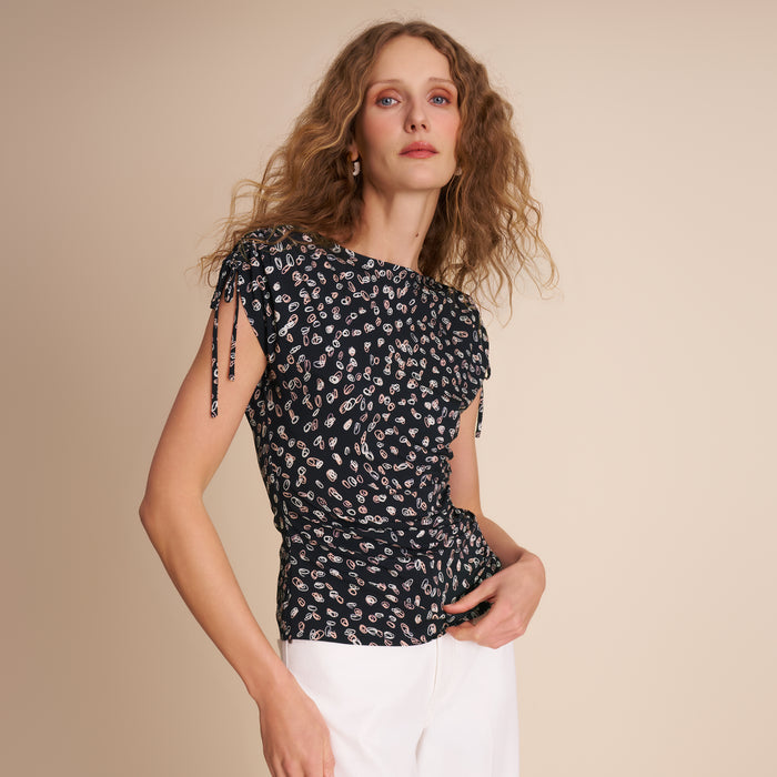 Woman wearing a black patterned top against a beige background |Exclude