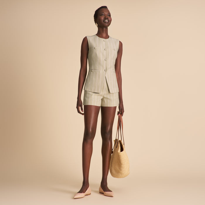 Woman wearing a light green sleeveless top and shorts set, holding a straw bag on a beige background