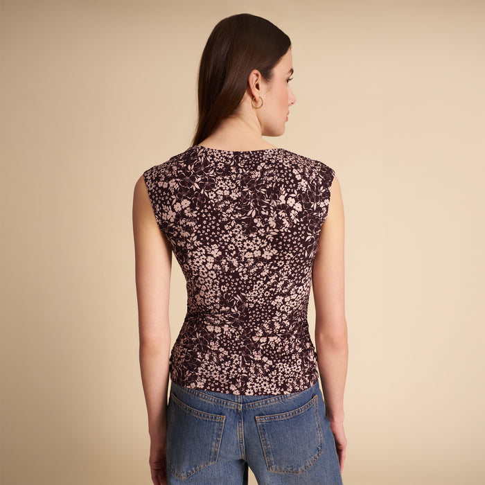 Woman wearing a floral sleeveless top and jeans on a beige background