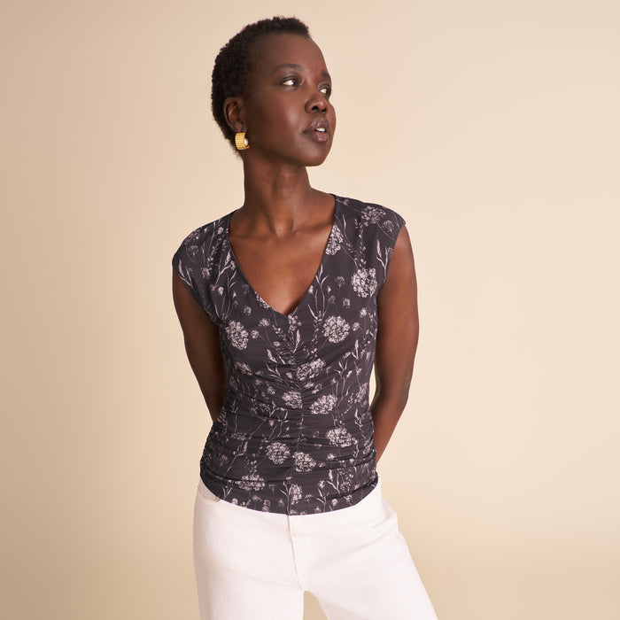 Woman wearing a floral top and white pants against a beige background | Lead