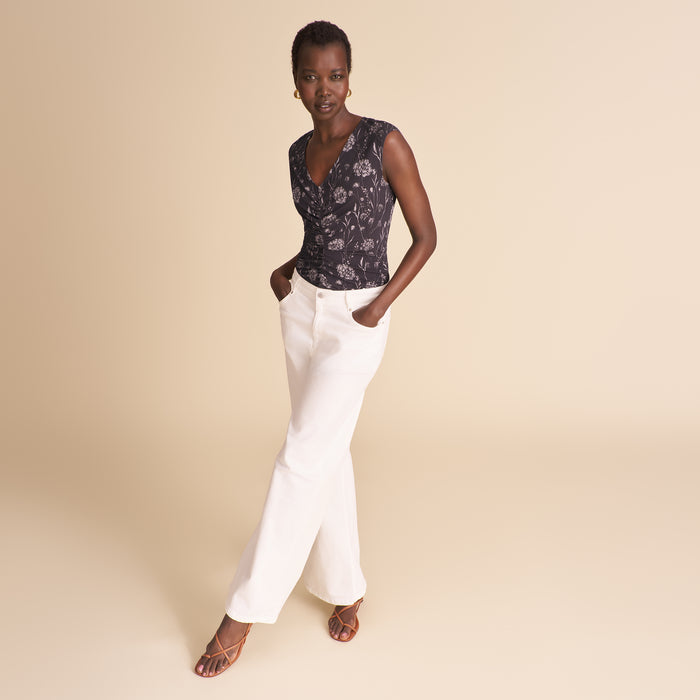 Woman wearing a floral top and white pants against a beige background