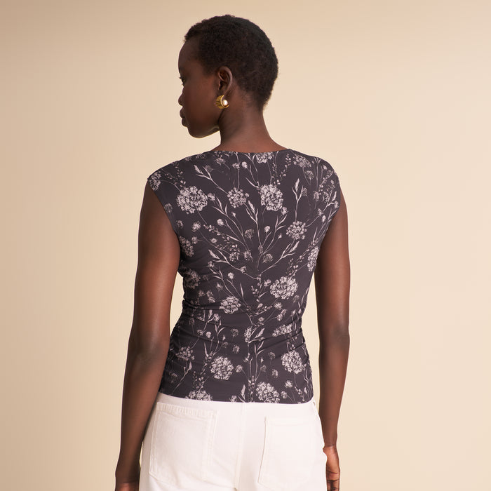Woman wearing a floral top and white pants against a beige background