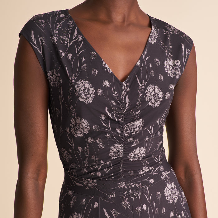 Woman wearing a floral top and white pants against a beige background