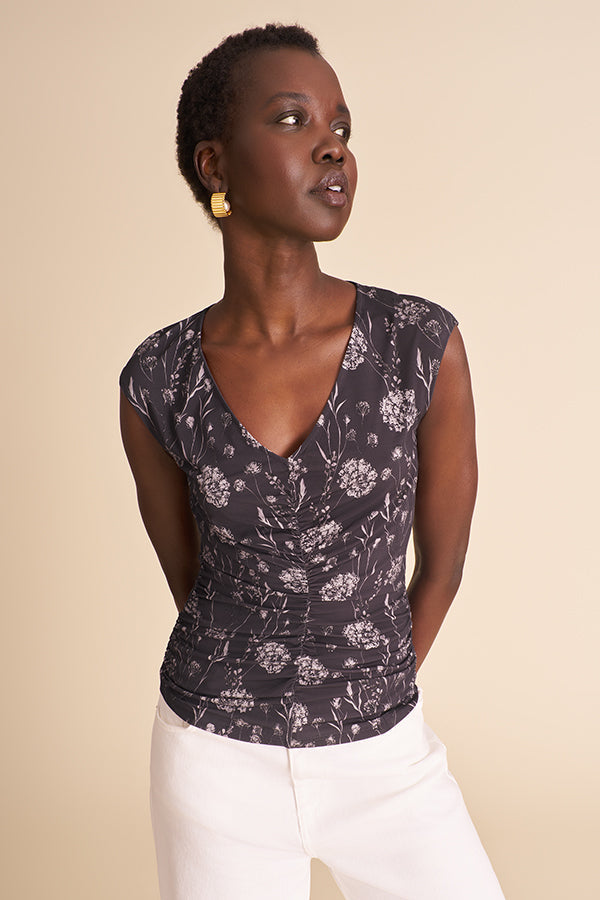 Woman wearing a floral top and white pants against a beige background | Exclude | Grid