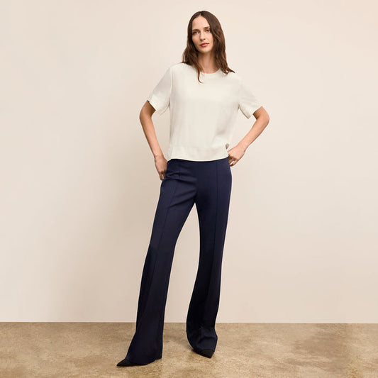 Woman wearing a white top and navy pants against a beige background | Lead