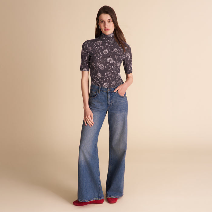 Woman wearing a patterned top and jeans on a beige background