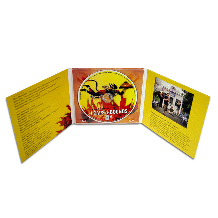 A yellow CD case by The Hanumen with a Leaps & Bounds CD inside. The open case shows Invocation song lyrics on the left and a photo of people, likely chanting Hare Krishna outside a building, on the right.