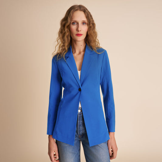 Woman wearing a blue blazer over a white top and jeans on a beige background | Lead