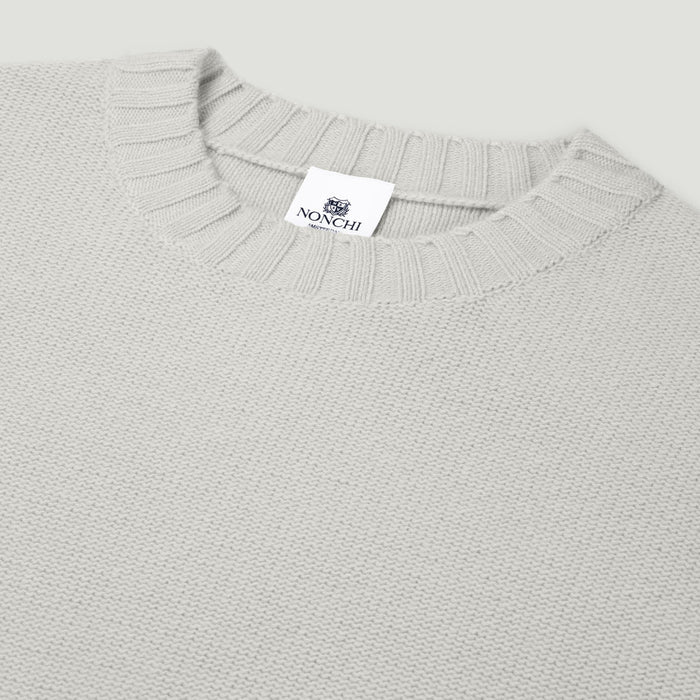 Close-up of a light gray sweater with a brand label on a light gray background