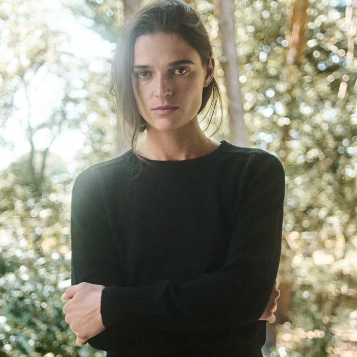 Woman wearing a black dress standing outdoors with greenery in the background
