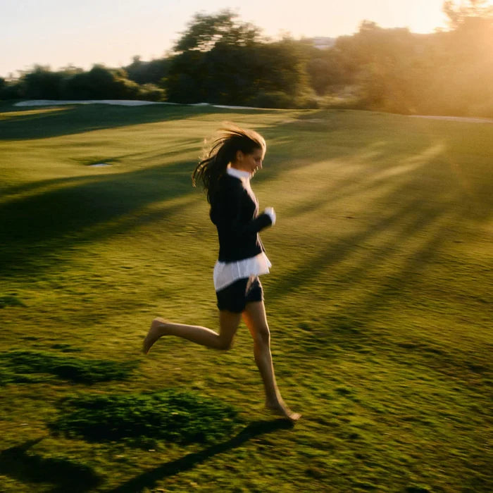Person running on a grassy field with sunlight casting long shadows