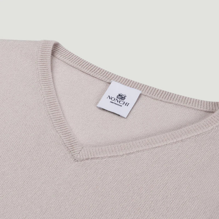 Close-up of a beige sweater with a brand label on a light gray background