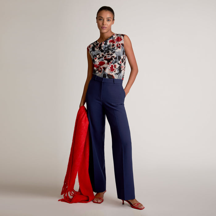 Woman wearing a floral top and blue pants with a red scarf, standing against a plain background | Exclude