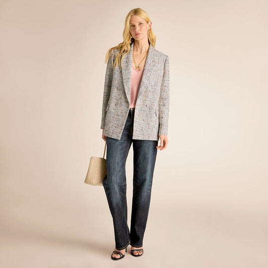 Woman wearing a gray blazer, pink top, and blue jeans on a beige background | Lead