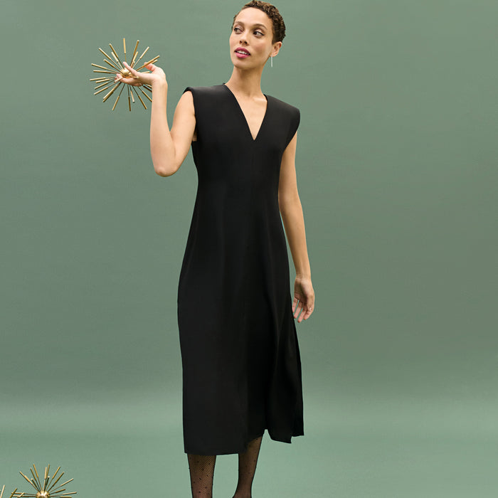 Woman in a black dress holding a decorative object against a green background | Exclude