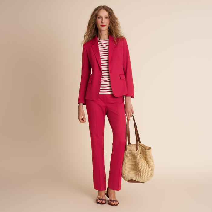 Woman wearing a red suit holding a beige handbag against a beige background