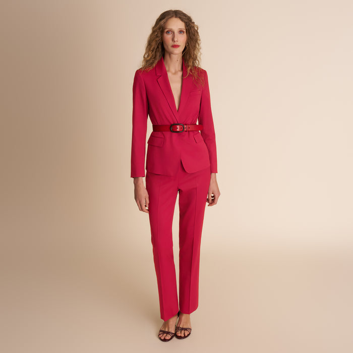 Woman wearing a red suit with a belt on a beige background