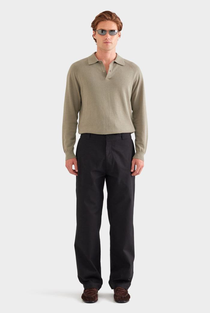 Man wearing a beige long-sleeve polo shirt and black pants on a white background